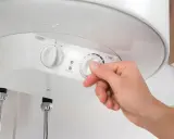 Mano ajustando el termostato de un termo eléctrico. Averigua cuanto dura un termo eléctrico y optimiza su uso.