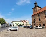 Rynek w Połajewie z zabytkowym ratuszem i kolorowymi kamienicami. Na brukowanym placu zaparkowane samochody.