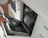Montaż frontu do zmywarki Whirlpool. Kobieta otwiera drzwi zmywarki z załadunkiem naczyń.
