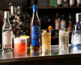 En bar med flera drinkar, inklusive en rosa drink, en gyllene drink med apelsin och körsbär, och en klar drink med oliv. Flera flaskor syns, bland annat en gin och en whisky. En perfekt kväll med en god bacardi drink.