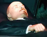 Mumia Lenina w garniturze i z krawatem w kropki, spoczywająca w szklanej gablocie.