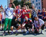 Grupa młodych ludzi w strojach piłkarskich, pozująca do zdjęcia. W tle budynki mieszkalne. To świetny **reto tekst** dla fanów futbolu.