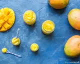 Délicieux curd mangue dans des petits pots, avec des mangues fraîches et des cuillères décorées. Un délice tropical !