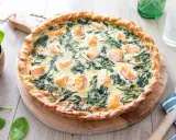 Une délicieuse quiche saumon épinard, dorée et garnie de morceaux de poisson et de légumes verts, prête à être dégustée.