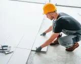 Fachowiec w żółtym kasku układa białe płytki. Zastanawiasz się, ile kosztuje położenie kafelek?
