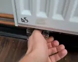 Ręka reguluje zawór grzejnika aluminiowego, próbując wyeliminować szum w grzejnikach aluminiowych.
