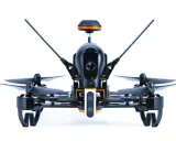 Ich sehe aus der **first person view** auf einen schwarzen Quadrocopter mit orangefarbenen Akzenten. Seine Kamera ist bereit für den Flug.
