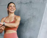 Glückliche Frau mit Sportuhr, die ihre Fortschritte nach 6 Monaten Training zeigt. Vorher-nachher-Erfolg.