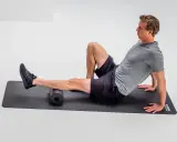 Mann rollt mit Schaumstoffrolle die Wade, um die Achillessehne zu dehnen.