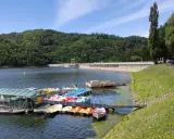 Jezioro Rożnowskie zaprasza na wodną trasę. Na pomoście czekają kolorowe rowerki wodne i łodzie, a w tle wznosi się imponująca zapora.