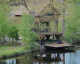 Drewniane domki wędkarskie nad jeziorem, otoczone zielenią, z pomostami schodzącymi do wody.