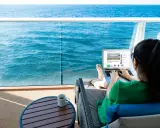 Donna su balcone di nave MSC lavora al laptop, con mare blu sullo sfondo. Scopri il pacchetto WiFi MSC e il suo costo per restare sempre connesso.