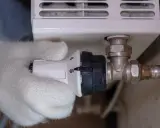 Main tenant ajuste le thermostat, réglant la température de son radiateur. Le raccord diélectrique montage est visible.