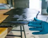 Main d'une personne en gant bleu manipulant un tissu de carbone imbibé de résine, une étape clé pour comprendre qu'est-ce que l'epoxy dans la fabrication composite.