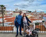 Familia disfrutando de las vistas de Lisboa con niños. Un bebé en portabebés y una niña en carrito, con la ciudad de tejados naranjas de fondo.