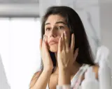 Donna preoccupata si tocca il viso, notando i segni dello stress sulla pelle.