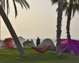 Entspannter Camping-Urlaub an der Costa del Sol. Palmen, Zelte, Sonnenschirme und eine Hängematte am Strand.