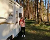 Kobieta z kubkiem kawy przy kamperze w lesie. Wspaniała przygoda z kamperem w Finlandii.
