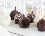 Deliciosos cake pops cubiertos de chocolate, algunos con chispas de colores y otros con glaseado blanco. Uno muestra su interior esponjoso.