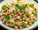 Pyszna sałatka z ciecierzycą, awokado i fetą, posypana płatkami chili i udekorowana natką pietruszki.