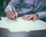 Dłoń pisze piórem na dokumencie, przygotowując się do wyrejestrowania auta online.