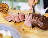 Perfekt grillad ryggbiff skärs upp på en skärbräda. Bredvid ligger en grillad citronhalva.