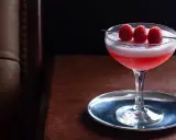 Ein eleganter Clover Club Cocktail mit Himbeeren auf einem silbernen Untersetzer, bereit zum Genuss.