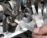 Mechanik sprawdza luzy zaworowe za pomocą szczelinomierza w silniku samochodowym.