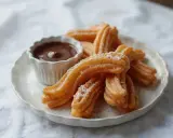 Churros co to? Złociste, chrupiące paluszki posypane cukrem pudrem, idealne do maczania w gorącej czekoladzie. Pyszna przekąska!