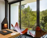 Chimenea encendida y sillones de cuero frente a un balcón con vistas a un bosque frondoso, ideal para el turismo interior España.