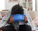Osoba z emetofobią przykryta kocem, pochylona nad niebieską miską, czuje się źle.