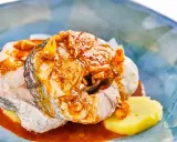 Merluza a la gallega con patatas y salsa de pimentón, servida en un plato azul.