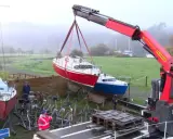 Grue soulevant un bateau rouge pour son recyclage. Un autre bateau bleu est posé sur des supports. L'opération de recyclage bateau se déroule dans un paysage brumeux.