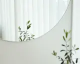 Odbicie gałązki oliwnej w okrągłym lustrze, które można łatwo przykleić do ściany. Białe zasłony w tle.