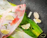 Cała ryba tilapia, przyprawiona chili i limonką, leży na zielonych liściach. Czy to tilapia, co to za ryba?