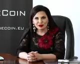 Rupert Ignatov, w czarnej koronkowej sukni z czerwonymi kwiatami, siedzi przy biurku.