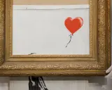 A framed Banksy artwork featuring a red balloon, hinting at how is Banksy rich.