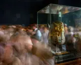 Goldene Maske des Pharao Tutanchamun in einer Vitrine, umgeben von verschwommenen Besuchern.