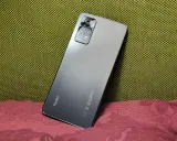 Elegancki, szary Redmi Note 11 Pro 5G Plus z aparatem 108MP na tle zielonej i bordowej tkaniny.