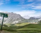 Wanderwegschild weist den Weg zum Refugio de Aliva und Espinama in den **Lagos de Covadonga**. Grüne Hügel und zerklüftete Berge unter blauem Himmel.