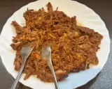 Delicioso pulled pork deshebrado en un plato blanco, listo para ser servido. Dos tenedores se clavan en la carne jugosa.