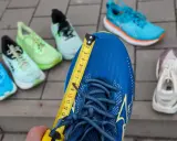 Miarka mierzy niebieski but do biegania. Czy buty do biegania powinny być większe? W tle inne kolorowe buty.