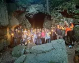 Grupa ludzi z latarniami przy skalnej grocie, odkrywająca tajemnice szlaku walońskiego.