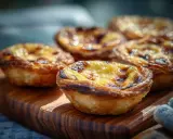 Fluffiga, gyllene pastel de nata på en träskärbräda. Krispiga kanter och krämig fyllning.