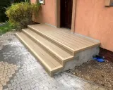 Jak zrobić schody z desek? Nowe, jasnobrązowe schody tarasowe z desek kompozytowych prowadzą do drzwi domu.