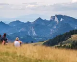 Para odpoczywa na trawiastym wzgórzu, podziwiając malownicze góry. To idealne miejsce, by zobaczyć w Szczawnicy zapierające dech w piersiach widoki.