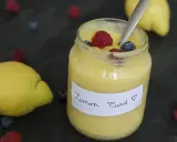 Un pot de lemon curd maison, garni de framboises et myrtilles, avec des citrons frais et des baies éparpillés.