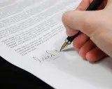 Podpisanie dokumentu, który może być upoważnieniem do rejestracji pojazdu. Długopis z piórkiem na białym papierze.