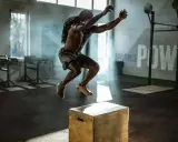 Mann mit Dreadlocks macht explosive Box Jumps in einem nebeligen Fitnessstudio.