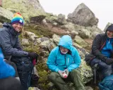 Vänner vilar på berg i snöfall, deras impregnerade jackor håller dem torra.